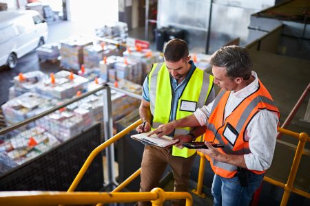 Shot of two warehouse workers standing on stairs using a digital tablet and looking at paperwork