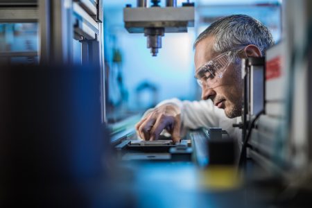 Mid adult male engineer examining machine part on a production line in a factory.